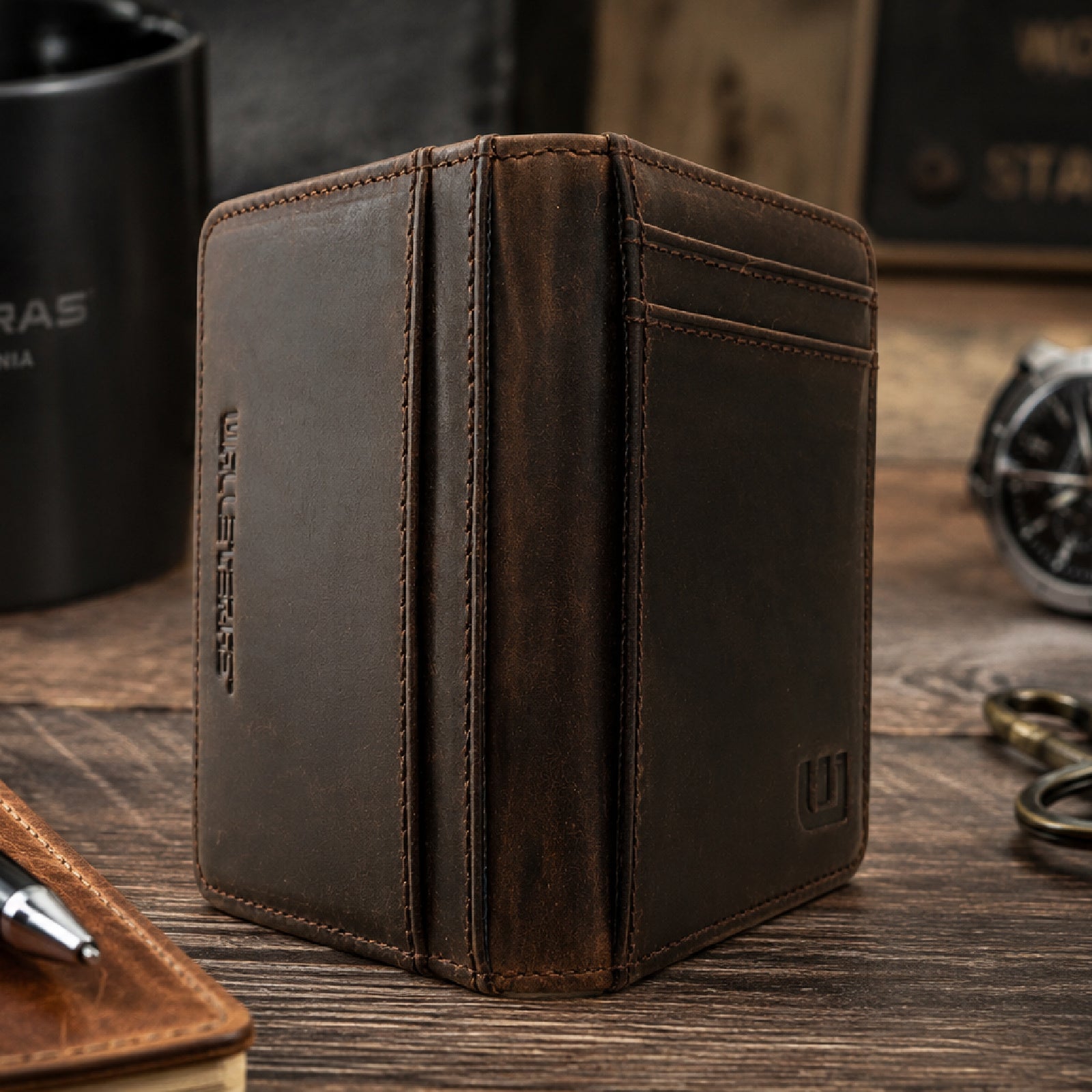 A dark brown distressed leather bi-fold wallet standing upright on a wooden table, with card slots on the front and an embossed vertical logo on the side.