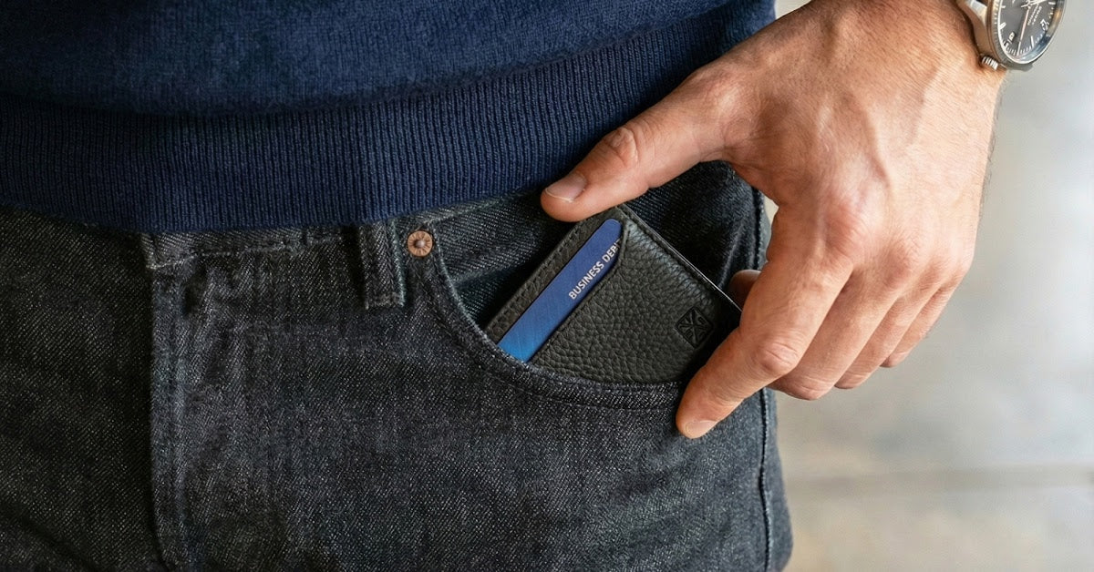 an image of a man in a blue sweater and dark jeans sliding his black wallet into the front pocket